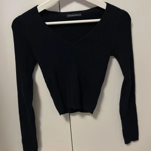 Svart ribbad topp från Brandy Melville - Säljer en svart ribbad topp från Brandy Melville med v-ringad hals och långa ärmar. Toppen har en slim passform och är tillverkad i mjukt material som sitter snyggt på kroppen. Perfekt för dig som gillar stilrena och enkla plagg.
