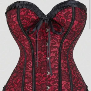 Röd och svart spetskorsett med snörning - Säljer en snygg korsett i röd och svart med spetsmönster och svarta satinband. Korsetten har snörning både fram och bak, samt dekorativa svarta volanger upptill och nedtill. Perfekt för dig som vill ha en statement piece med cool siluett och detaljer. Korsetten är från Shein i storlek L och är helt oanvänd, säljer då den tyvärr var för stor för mig 