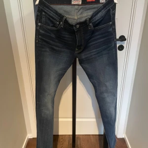 Crocker Skinny Jeans blå 32/32 - Snygga blå skinny jeans från Crocker med klassisk femficksdesign och bekvämt stretchigt tyg. Jeansen har en mörk tvätt med slitningar och kontrastsömmar, perfekt för en trendig och avslappnad look.