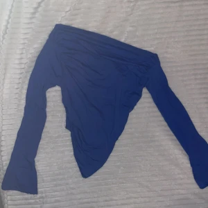 Blå offshoulder topp med långa ärmar - Säljer en snygg blå offshoulder topp med långa ärmar och tight passform. Toppen har en asymmetrisk skärning nedtill och är tillverkad i ett ganska så stretchigt, mjukt material som sitter skönt mot kroppen. 