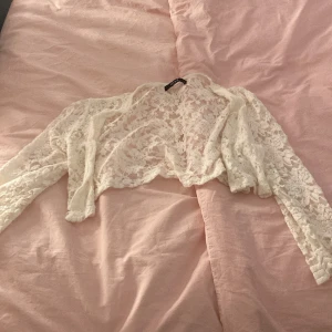 Vit spetsig bolerotopp från Vila 🤍🤍🤍 - Säljer en superfin vit bolerotopp från Vila i spets. Toppen är croppad och har lång ärm, perfekt att slänga över ett linne eller klänning. Den är genombruten med blommigt spetsmönster och känns både romantisk och trendig! 🫶🏻🤍🫶🏻🤍🫶🏻🤍