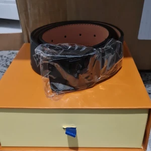 Svart L&V skärp i skinn - Snyggt svart bälte från L&V i äkta skinn med klassisk L&V-logga på spännet. Bältet har en stilren design och insidan är ljusbrun. Perfekt accessoar för att lyfta din outfit med en exklusiv touch.