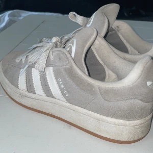Adidas Campus grå sneakers mocka - Grå Adidas Campus sneakers i mocka med vita detaljer och klassiska tre ränder på sidorna. Skorna har vit snörning, gummisula och rund tå. Adidas logga på plös och häl. Perfekta för en clean och stilren look. (det följer med nya vita snören)