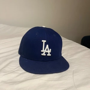Blå LA Dodgers keps från New Era - Säljer en klassisk blå LA Dodgers keps från New Era 59FIFTY-serien. Kepsen har broderad LA-logga i vitt framtill och är tillverkad i 100% polyester. Perfekt för dig som gillar sportig stil och vill ha en ikonisk look.