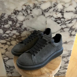  Alexander McQueen Oversize sneakers - Säljer ett par svarta sneakers från Alexander McQueen med chunky platt sula och ovandel i mocka. Skorna har svarta skosnören, rund tå och diskret logga på plösen. Perfekta för dig som gillar stilrena och trendiga sneakers med lite extra höjd. Använda vid två tillfällen, box samt kvitto finns ej pga tidigare flytt. ÄKTA skor inga kopior. 