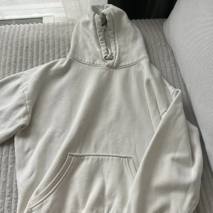 Vit hoodie med huva och ficka - En stilren vit hoodie med huva och snörning samt en stor magficka framtill. Tröjan har långa ärmar och är tillverkad i mjukt material, perfekt för en avslappnad look. 