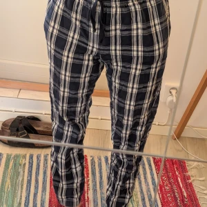 Rutiga byxor med snörning från Ellos - Mörkblå och vita rutiga byxor från Ellos i mjukt bomullstyg. Byxorna har elastisk midja med snörning och raka ben. Perfekta för en chill och avslappnad stil. Storlek 158/164 och passar mig som är 155