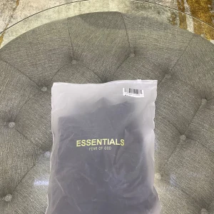 Svart Essentials Fear of God hoodie - Den är kopia1:1 Svart hoodie från Essentials Fear of God med stor logga på ryggen och mindre logga på bröstet. Klassisk känguruficka framtill, huva och ribbade muddar. Perfekt för en clean och stilren streetwear-look.