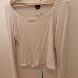 Vit ribbad långärmad topp Gina Tricot - Säljer en vit långärmad topp från Gina Tricot med ribbad struktur och rund, bred urringning. Toppen är i mjuk bomullsmix och har en enkel, clean look som passar till allt