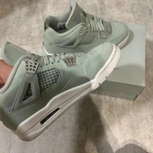Nike Air Jordan 4 Retro  - Säljer ett par mintgröna Nike Air Jordan 4 Retro med snygga silvriga detaljer och vit sula. Skorna har snörning, meshpaneler och är tillverkade i mocka för en lyxig känsla. Perfekta för dig som vill sticka ut med stilrena sneakers. Använda max 3 gånger, kvitto och låda finns till. Nypris 2800kr