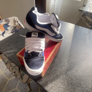 Vans knu skool  - Säljer ett par klassiska Vans Old Skool sneakers i marinblått och vitt. Skorna har vit sula, vit sidestripe och vita snören. Ovandelen är i mocka och canvas med tydliga kontrastsömmar. Perfekta för dig som gillar streetstyle och skatekänsla. Storlek 42 men passar upptill ca 44.5