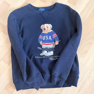 Mörkblå sweatshirt Polo Ralph Lauren - Mörkblå sweatshirt från Polo Ralph Lauren med ikoniska Polo Bear-trycket på bröstet. Tröjan har rund halsringning och långa ärmar. Perfekt för dig som gillar sportig och klassisk stil.