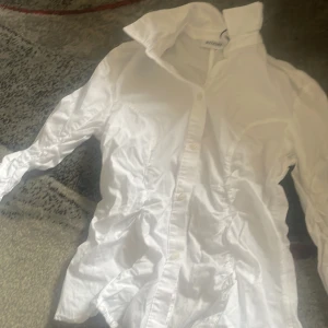 Vit skjorta från Weekday, strl 36 - Klassisk vit skjorta från Weekday i storlek 36. Skjortan har lång ärm med manschett och knappar framtill. Snygg krage och stilren design, perfekt att styla med jeans eller kjol. Tillverkad i mjuk bomull för en skön känsla.