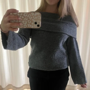 Grå offshoulder stickad tröja H&M - Mysig grå stickad tröja från H&M med bred offshoulder-krage och långa ärmar. Tröjan har en loose passform och är perfekt för kyligare dagar. Enkel att styla med både jeans och kjol.