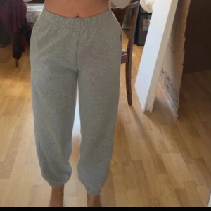 Grå mjukisbyxor med resår - Grå mjukisbyxor med resår i midjan och vid bensluten. Byxorna har en avslappnad passform och är tillverkade i mjukt bomullsmaterial, perfekta för chill dagar hemma eller till träning. Klassisk look utan synliga loggor eller detaljer.