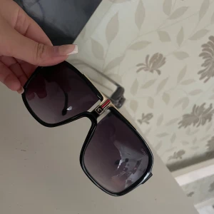 Svarta Carrera solglasögon med gulddetaljer - Säljer ett par snygga Carrera solglasögon med svart, fyrkantig ram och gulddetaljer vid bryggan. Glasen är mörka och har en lätt toning. Carrera-loggan syns på skalmen i guld. Ramen är i plast och har en cool retrovibe. kostar ny 1000 ungefär Har ingen box t dom tyvärr