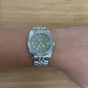 Seiko arabisk urtavla - Snygg Seiko automatisk klocka med silverfärgat armband i metall och rund boett. Urtavlan har arabiska siffror. Länken är klassisk jubilee-stil och bakboetten har ett transparent fönster som visar urverket. Perfekt för dig som gillar stilrena accessoarer.