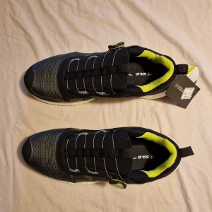 Solid Gear Vent 2 S1P - Svarta och neongula sneakers från Solid Gear, modell VENT 2. Skorna har BOA-snörning, meshpaneler och vit sula med neongul undersida. Ovandelen är i syntet och textil, med detaljer i svart och grått. Perfekta för dig som gillar sportig stil och smarta detaljer. Skoinlägg ingår.