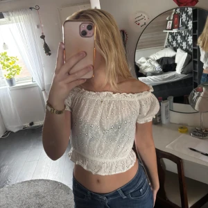 Vit offshoulder blus från Rut&Circle - Supersöt vit blus från Rut&Circle i storlek XS. Offshoulder-modell med korta puffärmar och broderade blommor över hela toppen. Croppad passform med volangkant nedtill och elastisk halsringning. Perfekt för vår och sommar, riktigt fräsch och feminin vibe.