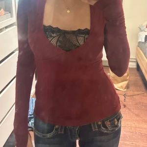 Vinröd långärmad topp Gina Tricot - Säljer en vinröd långärmad topp från Gina Tricot med djup v-ringning. Modellen är figurnära och har en enkel, stilren design utan mönster. Perfekt att styla med spets-bh under för en snygg layering-effekt.