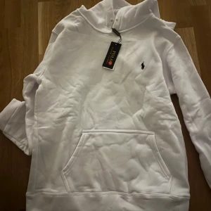 Vit hoodie från Polo Ralph Lauren S - Vit hoodie från Polo Ralph Lauren i storlek S. Klassisk design med huva, känguruficka och broderad logga på bröstet. Mjuk och skön bomull, perfekt för chill dagar. Långärmad och stilren, passar dig som gillar enkel och clean look.