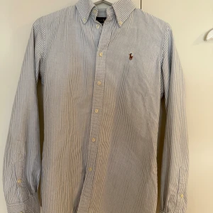 Randig skjorta från Ralph Lauren S - Klassisk skjorta från Ralph Lauren i vitt och blått med smala ränder och logga på bröstet. Långärmad och tillverkad i mjuk bomull. Storlek S, men custom fit så passar XS.