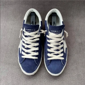 Blå Golden Goose sneakers med stjärna - Snygga sneakers från Golden Goose i mörkblå mocka med vit stjärndetalj på sidan och vita snören. Skorna har rund tå, platt sula och vit hälkappa. Perfekta för dig som gillar en cool och avslappnad stil.