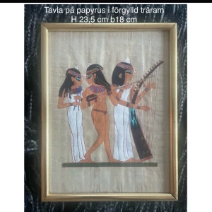 Egyptisk Handmålad tavla- Äkta Papyrus- Förgylld vintage ram- 1970/80- tal - En vacker handmålad tavla utförd på äkta papyrus med ett klassiskt egyptiskt motiv. Den föreställer tre kvinnor som dansar och spelar instrument. Hathor var namnet på musiken, dansen och glädjens gudinna. Tavlan är i mycket gott skick och är den perfekta presenten till någon som samlar på egyptisk konst eller bara vill inreda med lite mer karaktäristiska detaljer i hemmet. Mått: H 23,5 cm B 18 cm