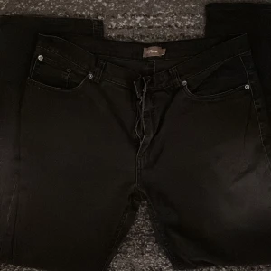 Svarta jeansbyxor från MyWear - Svarta jeansbyxor från MyWear med klassisk femficksdesign. Byxorna är tillverkade i 98% bomull och 2% elastan för en bekväm passform. De har raka ben och bälteshällor, samt dragkedja och knapp framtill. Perfekta för en stilren och enkel look.