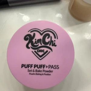 KimChi Chic Puff Puff Pass puder - KimChi Chic Puff Puff Pass Set & Bake Powder i färgen PPP 01 Ivander. Löst puder med en ljus elfenbensnyans och en hint av lavendel. Kommer i en rund burk med rosa lock och svart text. Perfekt för att fixera sminket och ge en matt finish.