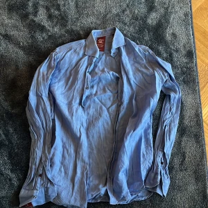 Blå skjorta från Castor Pollux - Säljer en stilren blå skjorta från Castor Pollux i slim fit-modell. Skjortan har klassisk krage, långa ärmar med manschett och knappar framtill. Perfekt för dig som gillar en enkel men snygg look.