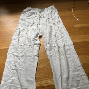 Vita linnebyxor med snörning och hög midja  - Luftiga vita linnebyxor med breda ben och snörning i midjan. Perfekta för varma dagar och ger en avslappnad vibe. Elastisk midja för extra komfort och enkel passform.