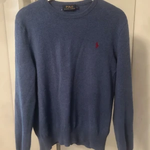 Blå kashmirtröja Polo Ralph Lauren  - Mysig blå kashmirtröja från Polo Ralph Lauren med rund halsringning och klassisk röd broderad logga på bröstet. Tröjan har lång ärm och ribbade muddar för en snygg passform. 