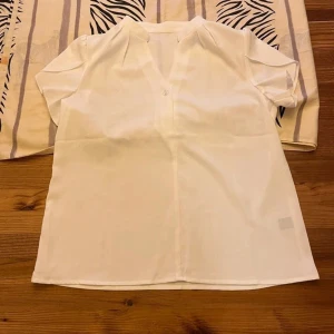 Vit Blus  - Säljer en stilren vit blus som är helt oanvänd. Perfekt för båda vardagsbruk och mer formella tillfällen. 