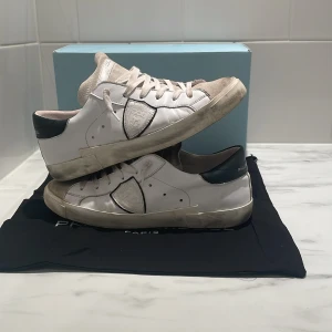 Philippe Model - Snygga vita sneakers från Philippe Model med detaljer i grå mocka på tån och svart hälparti. Skorna har snörning, rund tå och är tillverkade i skinn med en klassisk låg siluett. Perfekta för dig som gillar stilrena och trendiga sneakers.