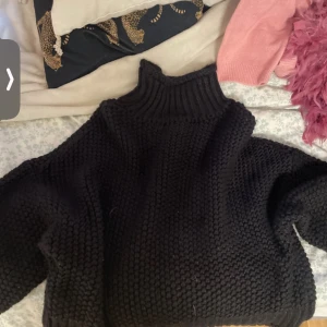 Svart stickad polotröja oversized - Mysig svart stickad polotröja med oversized passform och grovstickat mönster. Tröjan har långa ärmar och hög krage som ger en cool och avslappnad vibe. Perfekt för kalla dagar när du vill vara både varm och snygg.