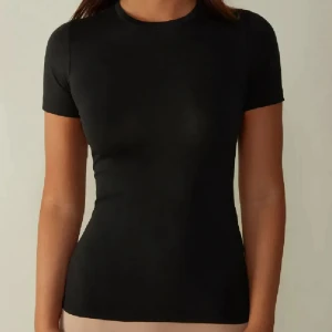 Intimissimi T-shirt - Enkel och stilren svart t-shirt med tight passform och korta ärmar. Perfekt basplagg med rund halsringning, passar till allt och är lätt att matcha. Materialet känns mjukt och följsamt mot kroppen.
