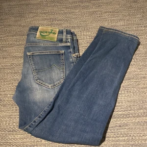 Blå jeans från Jacob Cohën - Snygga blå jeans från Jacob Cohën med klassisk femficksdesign, ljusa slitningar och gröna detaljer på knapp och patch. Jeansen har raka ben och normal passform, tillverkade i mjukt denimtyg för en bekväm känsla. Modell (style 622) Storlek 30.                                  Tveka på inte att ställa frågor eller fråga om fler bilder