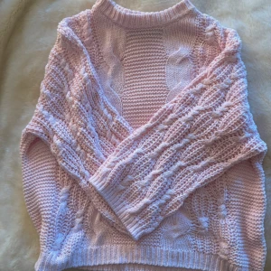 Rosa stickad tröja  - Superfin ljusrosa stickad tröja från Vero Moda med flätstickat mönster och ribbade muddar. Tröjan har en klassisk rund halsringning och långa ärmar. 