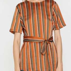 Randig blus topp från Koton - Säljer en snygg topp från Koton i orange med vita och gröna ränder. Toppen har korta ärmar, rund halsringning och ett matchande knytbälte i midjan. Perfekt för dig som gillar färg och mönster! Materialet känns lätt och skönt mot huden.