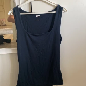 Mörkblå linnetopp från 157 XS - En enkel och stilren mörkblå linnetopp från 157 i storlek XS. Toppen har breda axelband och rundad halsringning. Tillverkad i mjuk och stretchig viskosblandning som sitter skönt mot kroppen. Perfekt att matcha med jeans eller kjol.