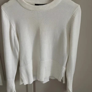 Vit stickad tröja med vida ärmar - Säljer en vit stickad tröja med bred ribbad kant nertill och på ärmsluten. Tröjan har rund halsringning och långa, lite vidare ärmar med slits som ger en snygg och trendig look. Perfekt att matcha med jeans för en clean stil. (Använd två gånger)