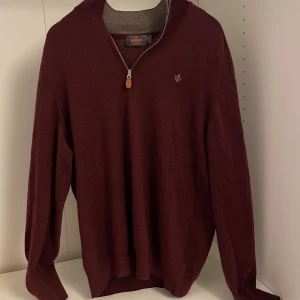 Vinröd merinoullströja från Morris M/L - Vinröd långärmad tröja från Morris i 100% merinoull. Tröjan har en stilren half zip-dragkedja med läderdetalj och liten broderad logga på bröstet. Perfekt för dig som gillar klassisk och snygg stil med en modern touch. Står att strl är XL men den har krympt i tvätten som lett till att den är M/L i storleken. Annars är den i väldigt bra skick. Nypris 1799kr