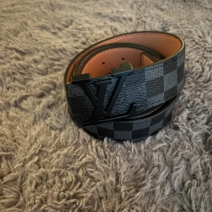 rutigt svart bälte - Snyggt svart bälte med klassiskt rutigt mönster. Bältet är gjort i exklusivt skinn med beige insida och har en stilren design som sticker ut. Perfekt accessoar för att lyfta din outfit.