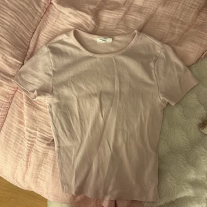 Ljusrosa t-shirt från ginatricot - Enkel och stilren ljusrosa t-shirt från gina. Modellen är klassisk med rund halsringning och korta ärmar. Tillverkad i mjuk bomull som känns skön mot huden. Perfekt för en clean och avslappnad look.