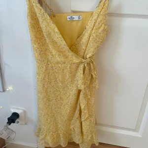Ljusgul klänning - Ljusgul klänning med små blommor och knyt & volang på sidan, storlek xs från hollister.