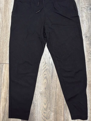 Svarta byxor från Only XS - Svarta byxor från Only i storlek XS med tapered passform och dragsko i midjan. Byxorna har resår bak, bälteshällor och fickor fram, enbart fickor för designs skull där bak dvs inte riktiga. Tillverkade i mjukt material som känns skönt mot huden.