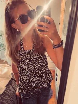 Svart blommig bandeau topp - Supersöt bandeau topp i marinblått med vitt blommönster. Toppen är ärmlös och har volangdetaljer som ger en luftig och somrig känsla. Går att styla på massa olika sätt, både som topp  men även som kjol. Materialet känns lätt och passar perfekt för varma dagar. Strlk 34 / S