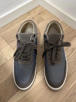 Bruna och grå sneakers från Garment Project - Snygga sneakers från Garment Project i brunt och grått med ovandel i mocka och mesh. Skorna har rund tå, vita sulor och klassisk snörning. Perfekta för dig som gillar stilrena och moderna detaljer.