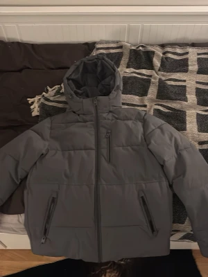 Grå pufferjacka från Jack & Jones - Säljer en grå pufferjacka från Jack & Jones i storlek XS men kan upplevas som S. Jackan har huva, tre dragkedjeförsedda fickor och en clean look utan mönster. Perfekt för kalla dagar och riktigt skön att bära. Passar dig som gillar enkel och stilren design.